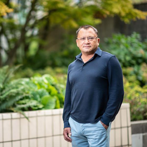 Dr. Artem Cherkasov standing outside in front of a low wall and greenery