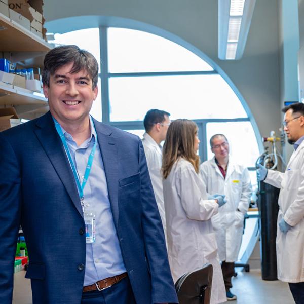 Dr. François Bénard with researchers wearing lab coats in a lab behin dhim